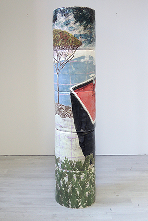 A ceramic column or tube with a landscape painted on it inside a white gallery space. 
